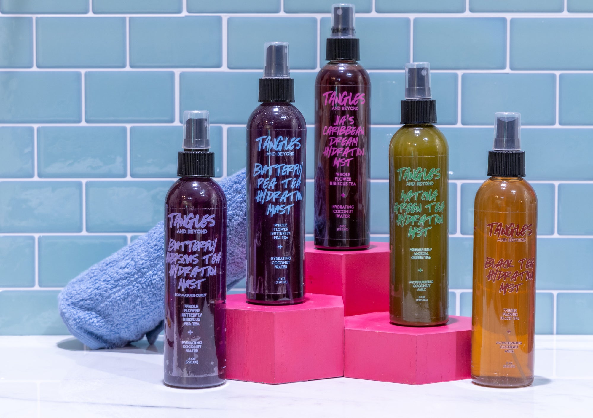 Group picture of Tangles and Beyond Hydration Mists standing on pink boxes with blue towel on blue tiled background 