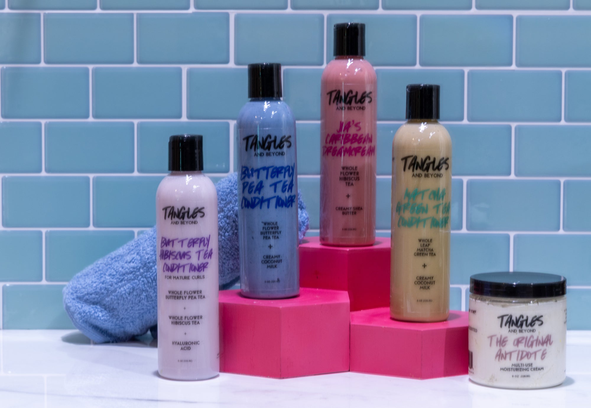 Group of flower infused conditioners by Tangles and Beyond with blue towel on blue tiled background.