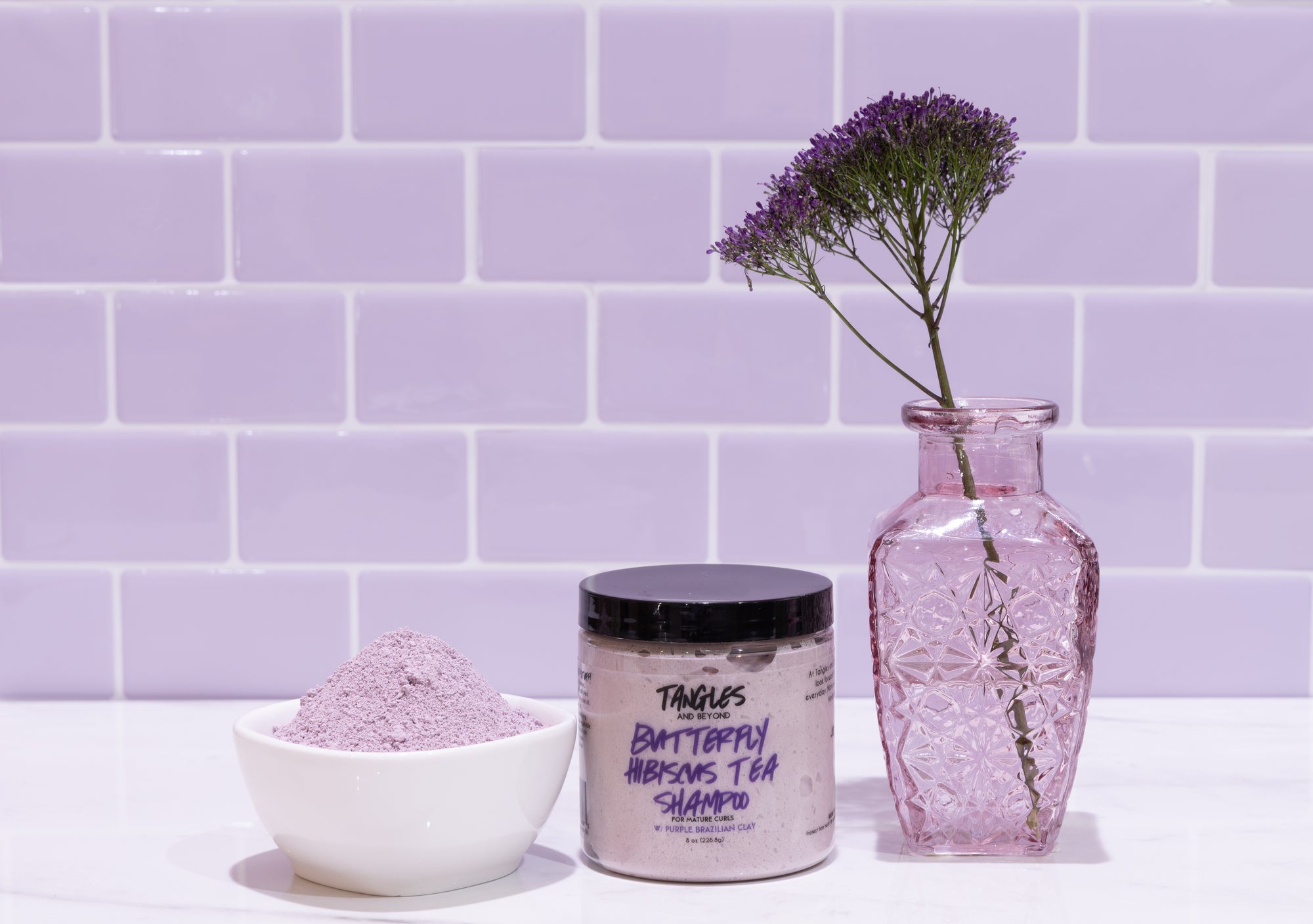Tangles shampoo and powder with a vase against a purple tiled wall