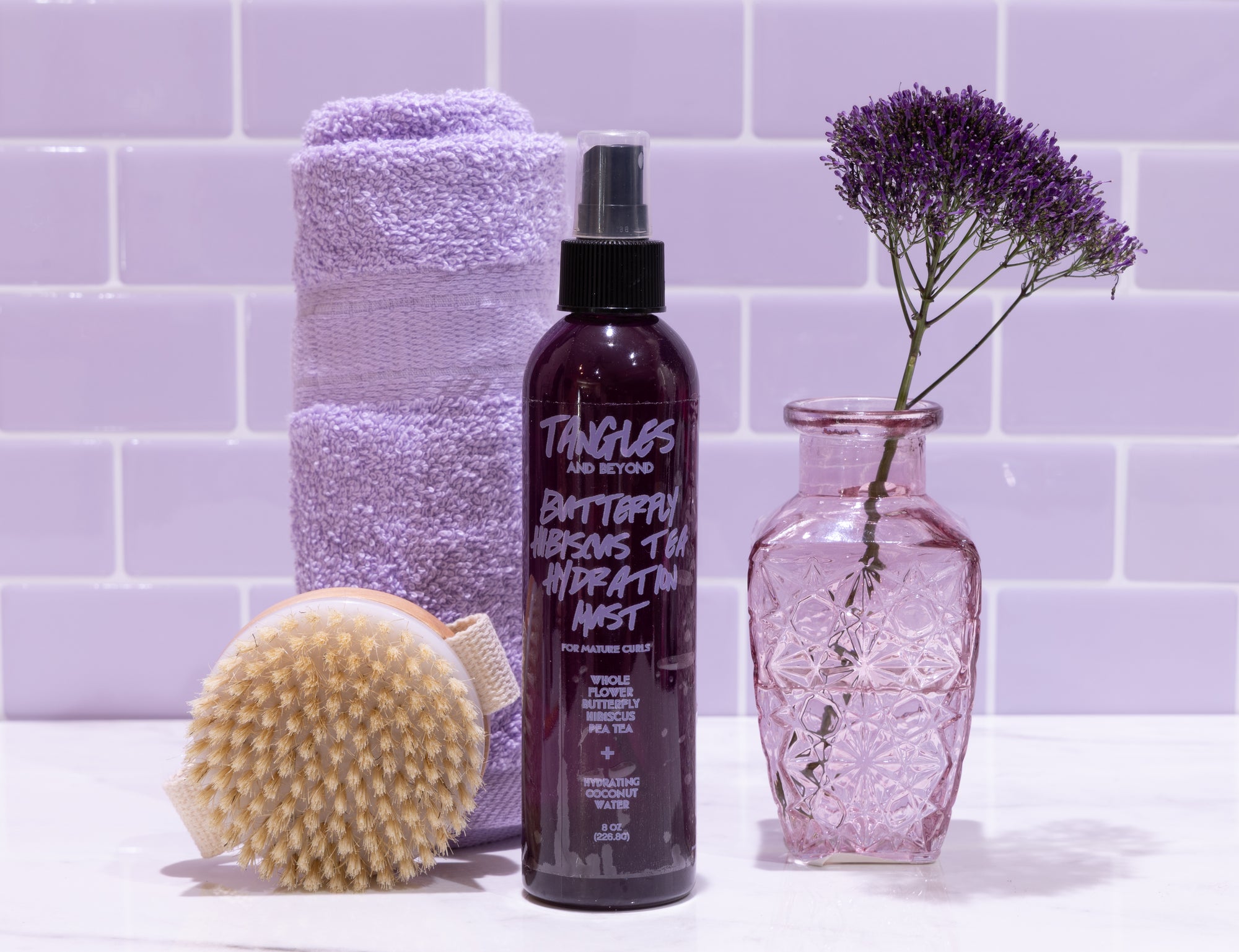 Bottle of 'Tangles and Beyond' product with a brush, towel, and vase on a tiled bathroom wall background.