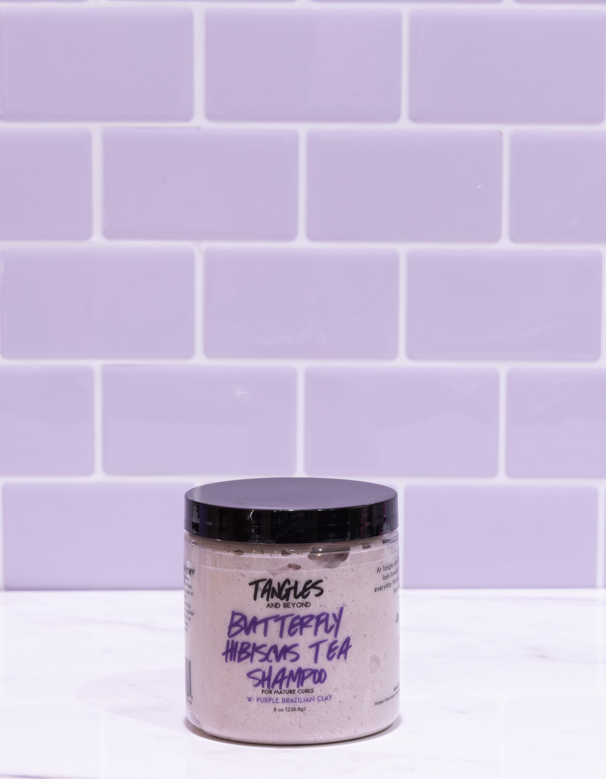 Jar of Tangles Butterfly Hibiscus Tea Shampoo against a purple tiled wall
