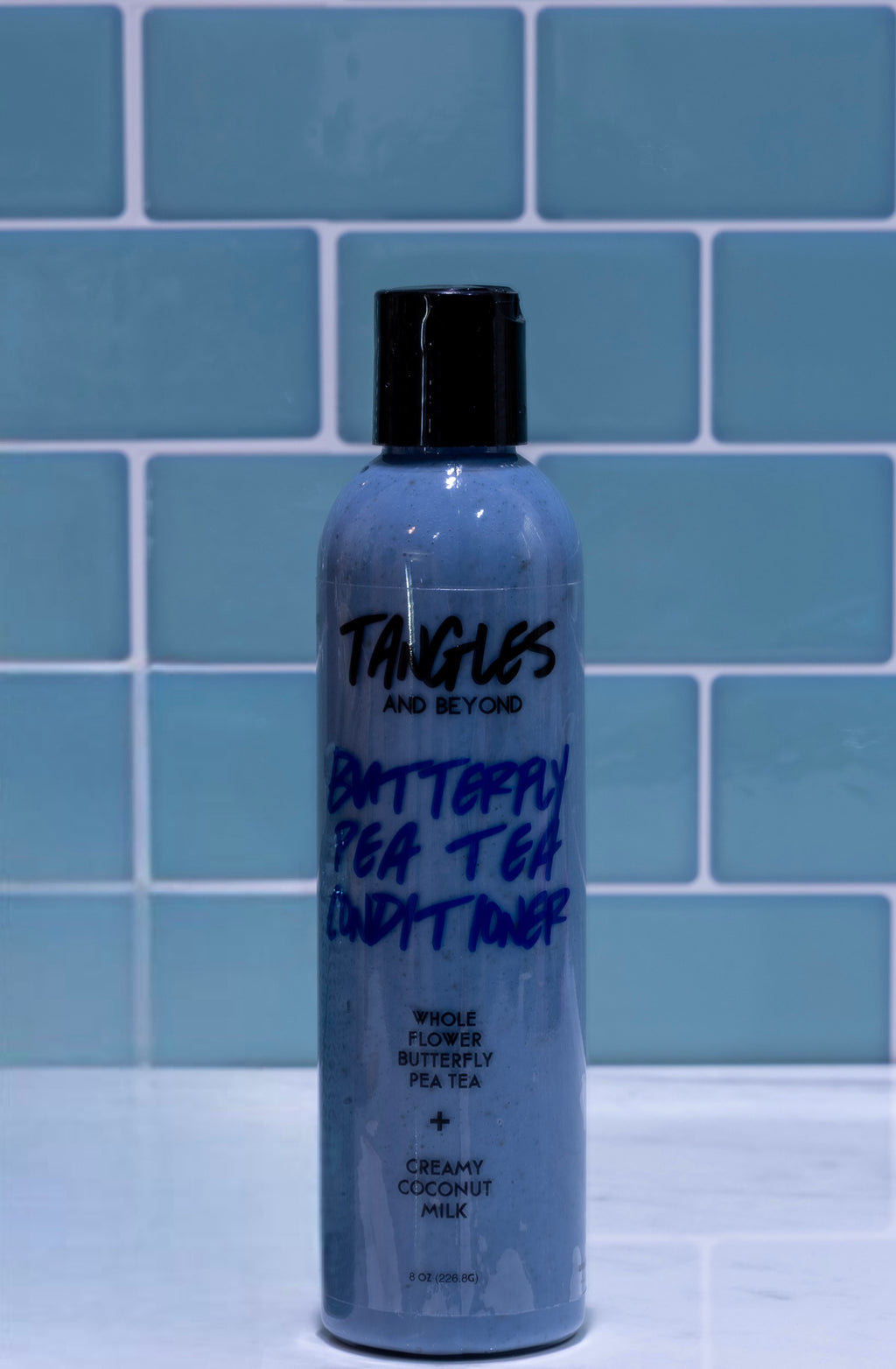 Bottle of 'Tangles and Beyond Butterfly Pea Tea Lush Toner' against a blue tiled wall.
