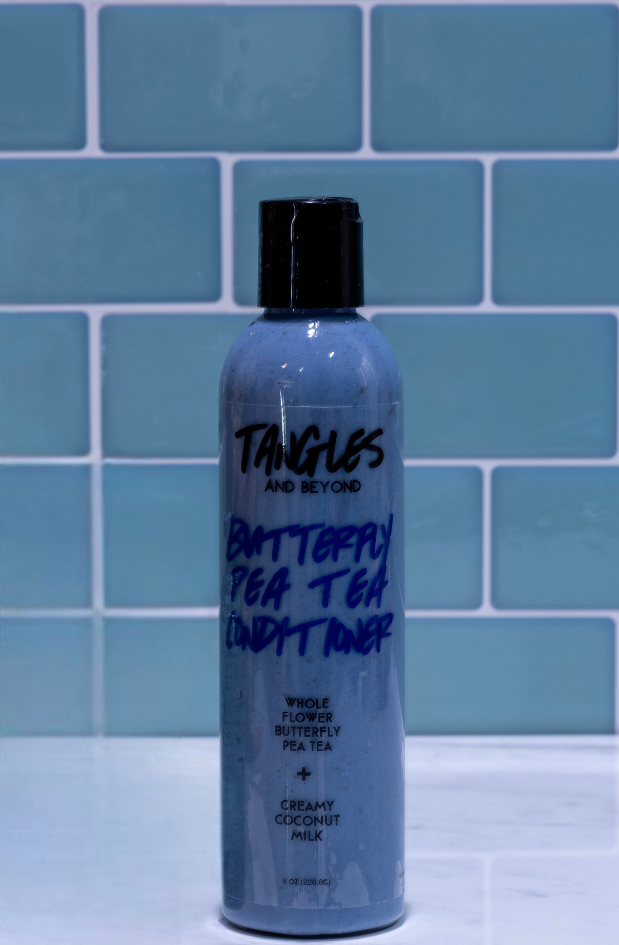 Bottle of 'Tangles and Beyond Butterfly Pea Tea Lush Toner' against a blue tiled wall.