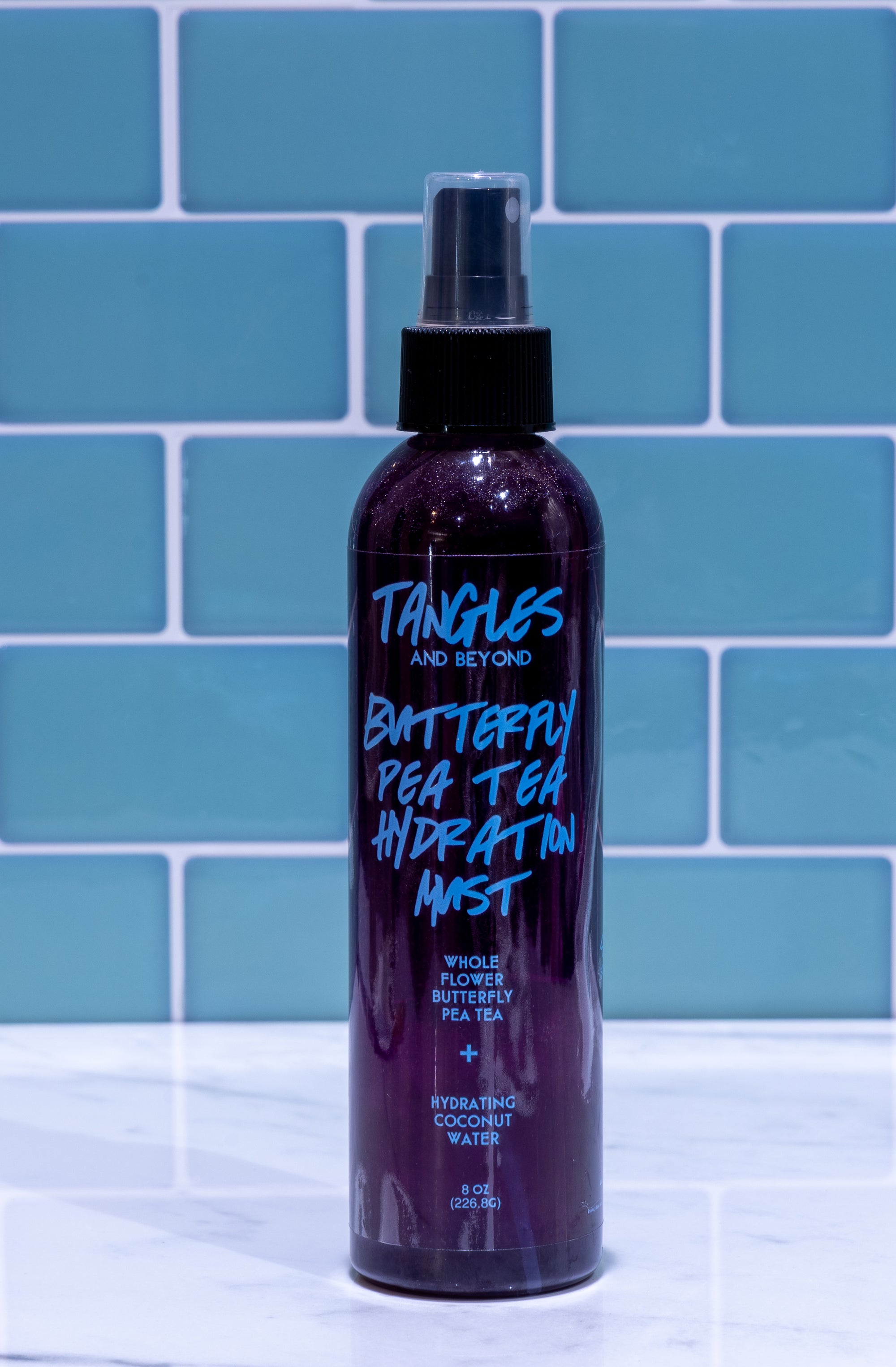 Bottle of 'Tangles and Beyond' hair product on a tiled surface with blue tiles in the background.