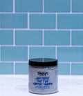 Jar of shampoo with blue label against a blue tiled wall