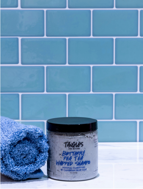 Jar of Tangles shampoo with a blue towel against a blue tiled wall