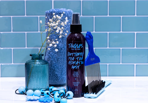 Hair care products including a spray bottle and comb against a blue tiled wall.