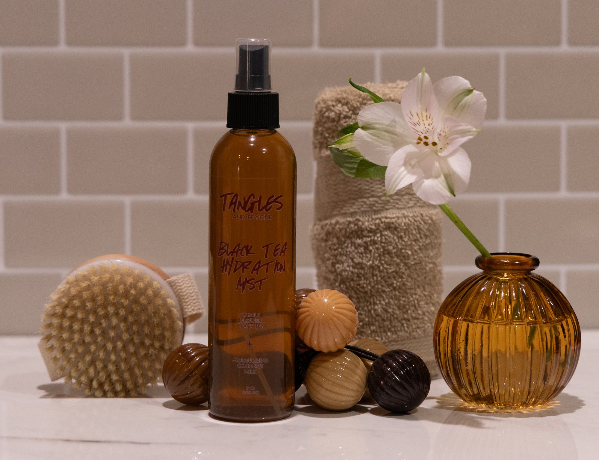 Brown bottle labeled 'Tangles' with a white flower, towel, and decorative items on a tiled bathroom counter.