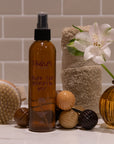 Brown bottle labeled 'Tangles' with a white flower, towel, and decorative items on a tiled bathroom counter.