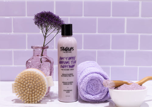 Bath and body products on a white surface with a purple tiled wall background
