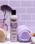 Bath and body products on a white surface with a purple tiled wall background