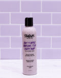 Bottle of Tangles and Co conditioner on a white surface with a purple tiled wall background