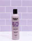 Bottle of Tangles and Co conditioner on a white surface with a purple tiled wall background