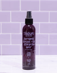 Purple spray bottle labeled 'Tangles and Beyond' on a white surface with purple tiled wall background
