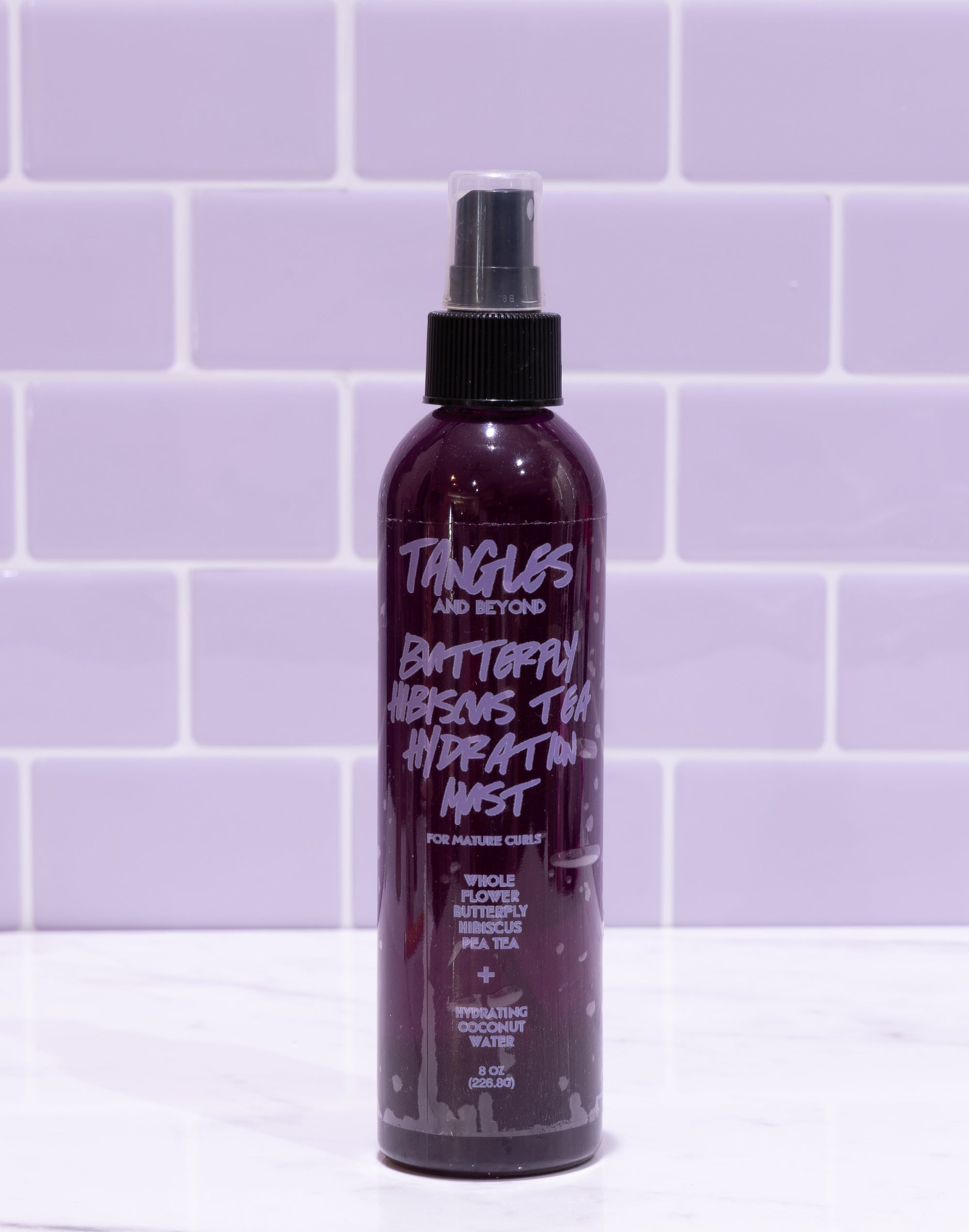 Purple spray bottle labeled 'Tangles and Beyond' on a white surface with purple tiled wall background
