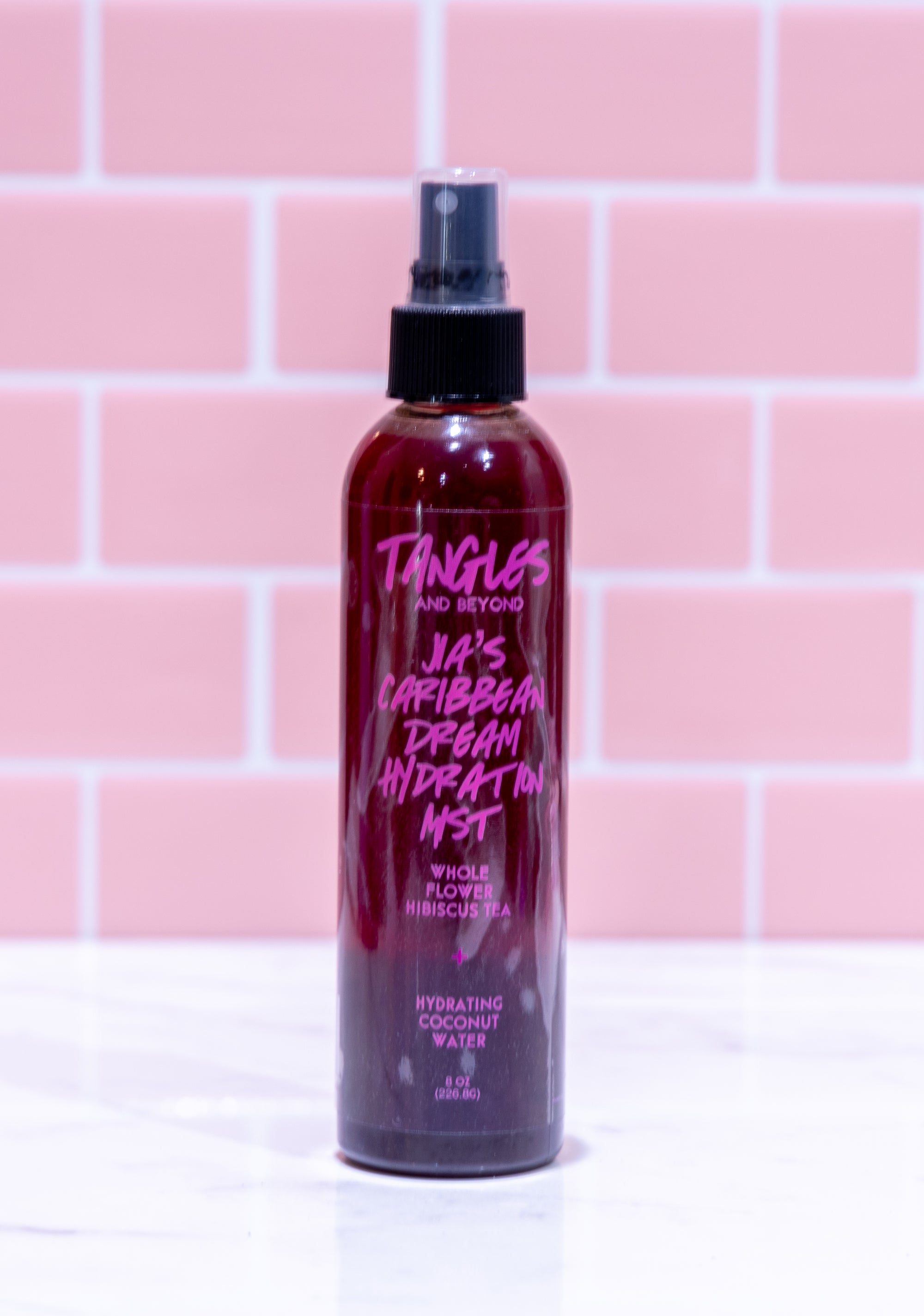 Bottle of Tangles & Beyond hair product with pink text on a pink tiled background