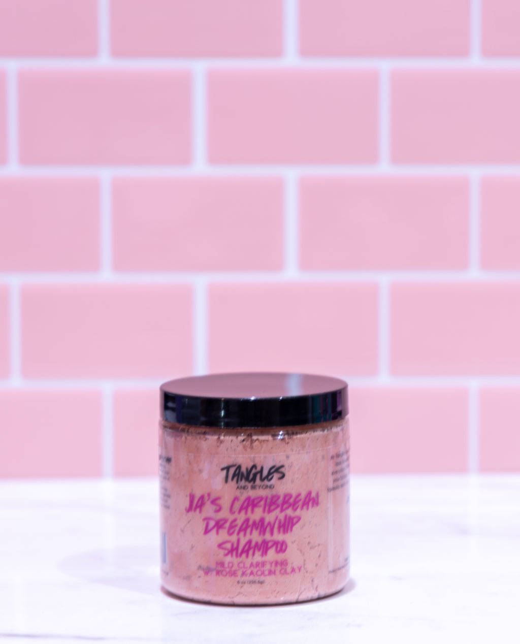 Jar of shampoo with visible branding against a pink tiled wall