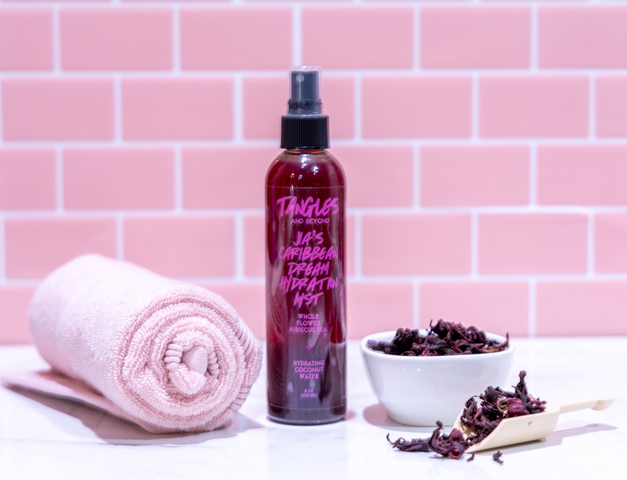 Tangles hair product bottle with a towel and bowl on a pink tiled background