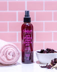 Tangles hair product bottle with a towel and bowl on a pink tiled background