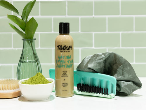 Tangles hair care products including a bottle, brush, and scrunchie on a green tiled wall background.