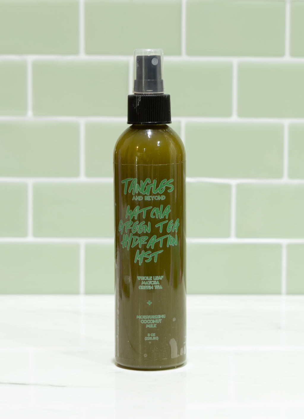 Green spray bottle with black nozzle on a light green tiled wall background