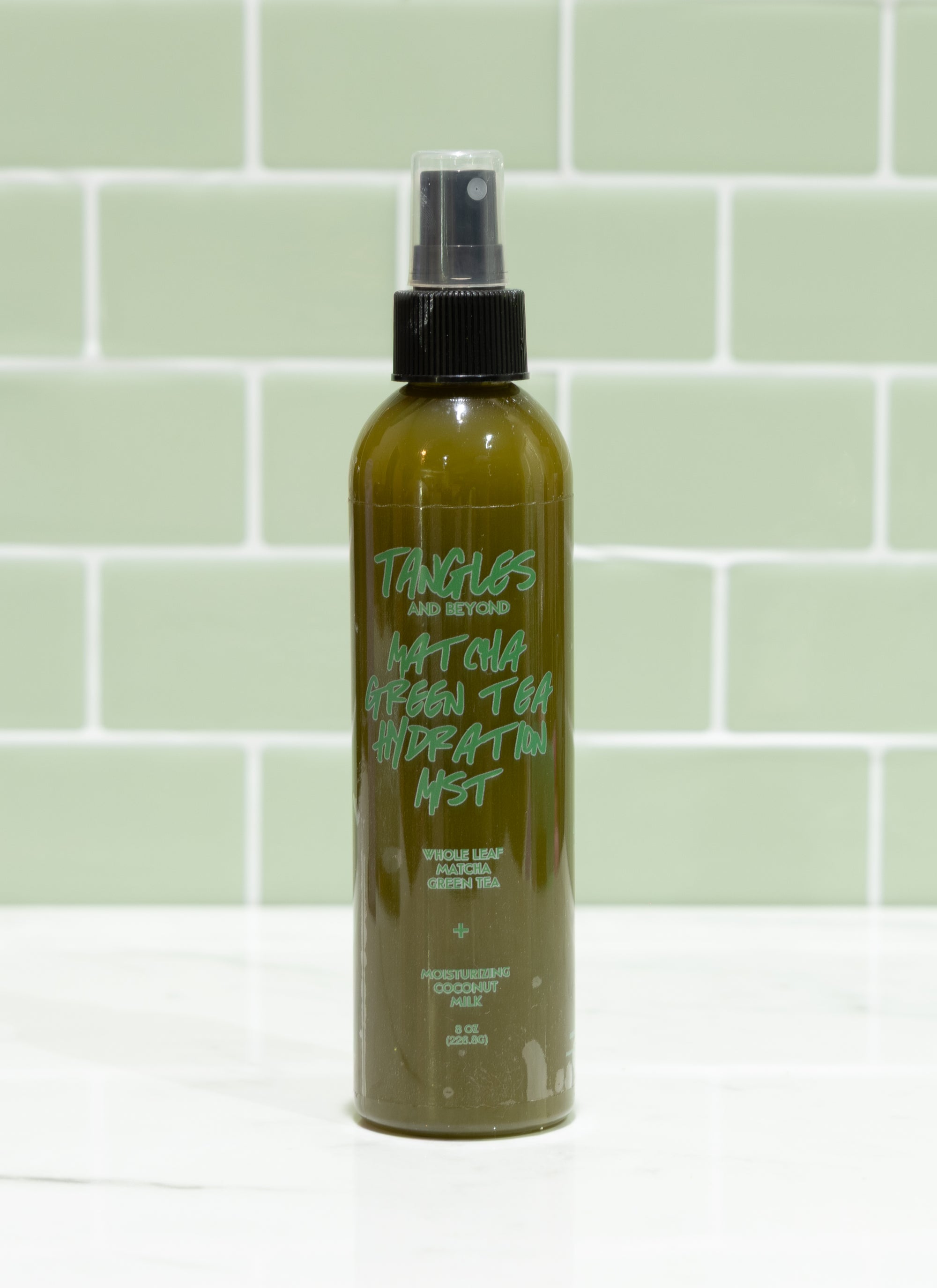 Green spray bottle with black nozzle on a light green tiled wall background