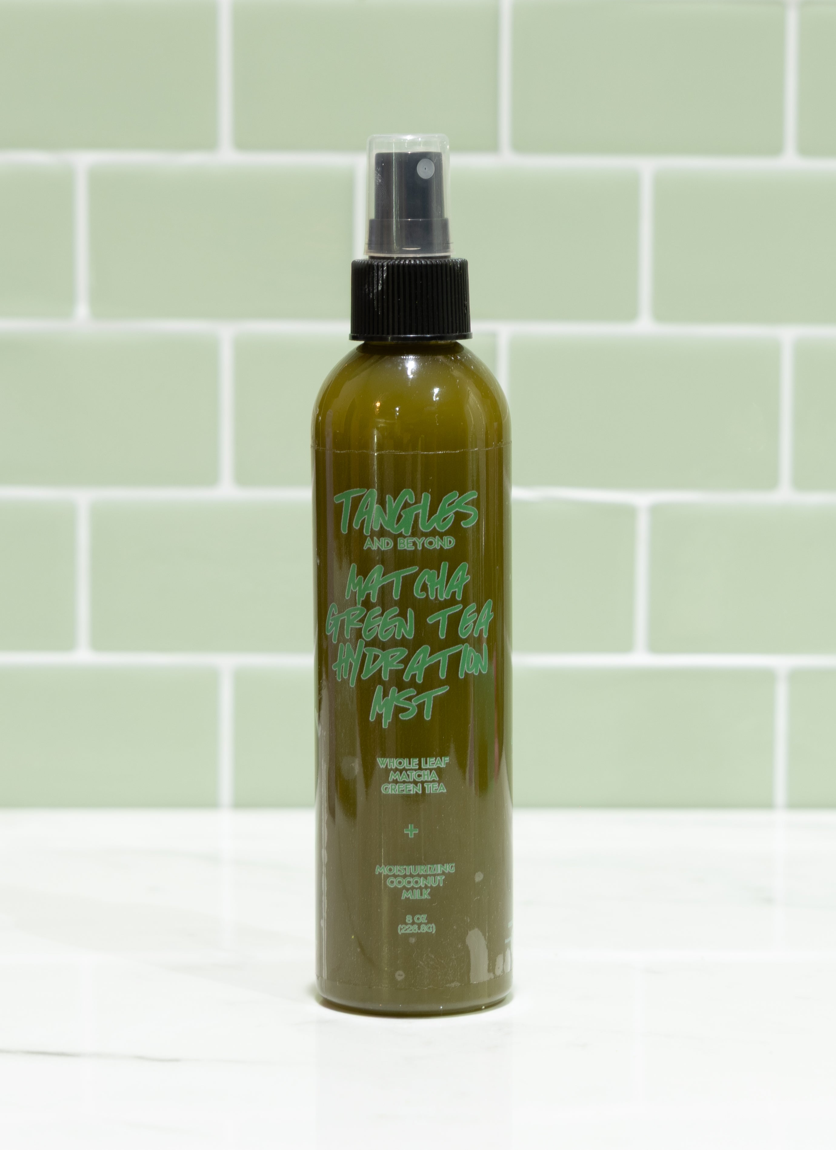 Green spray bottle with black nozzle on a light green tiled wall background
