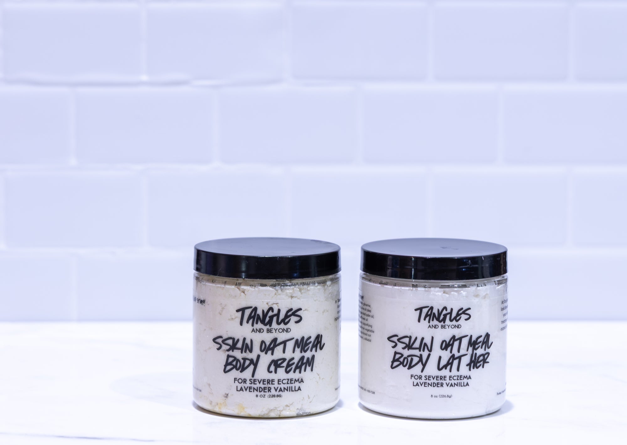 Two jars of Tangles and Beyond Skin Oatmeal Body Cream on a white tiled background