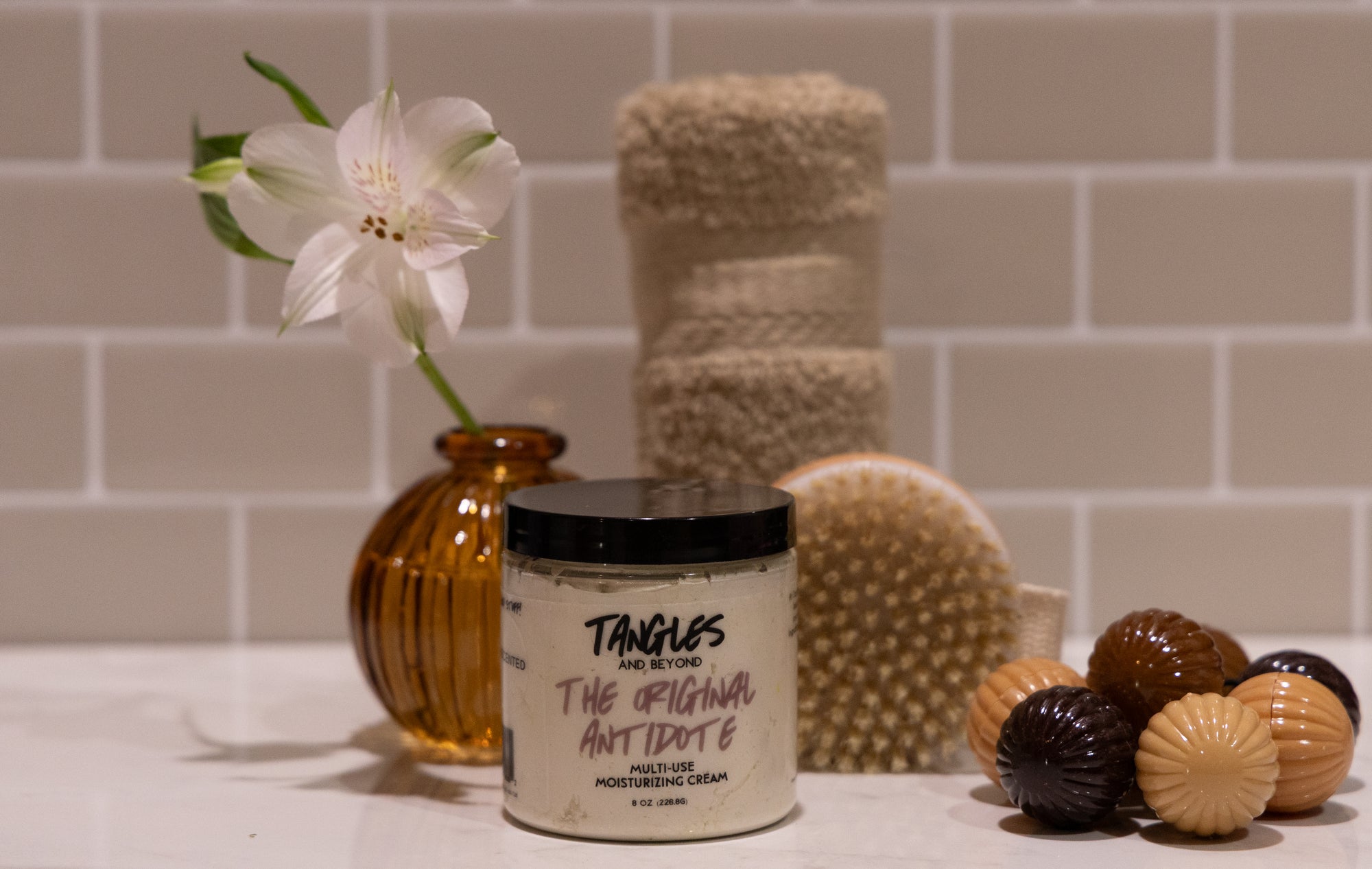 Jar of Tangles body scrub with a flower and bath items on a tiled surface