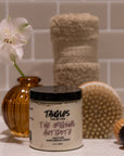 Jar of Tangles body scrub with a flower and bath items on a tiled surface